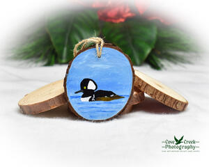 A hand-painted hooded merganser on water wood slice ornament available for purchase at Cove Creek Photography.
